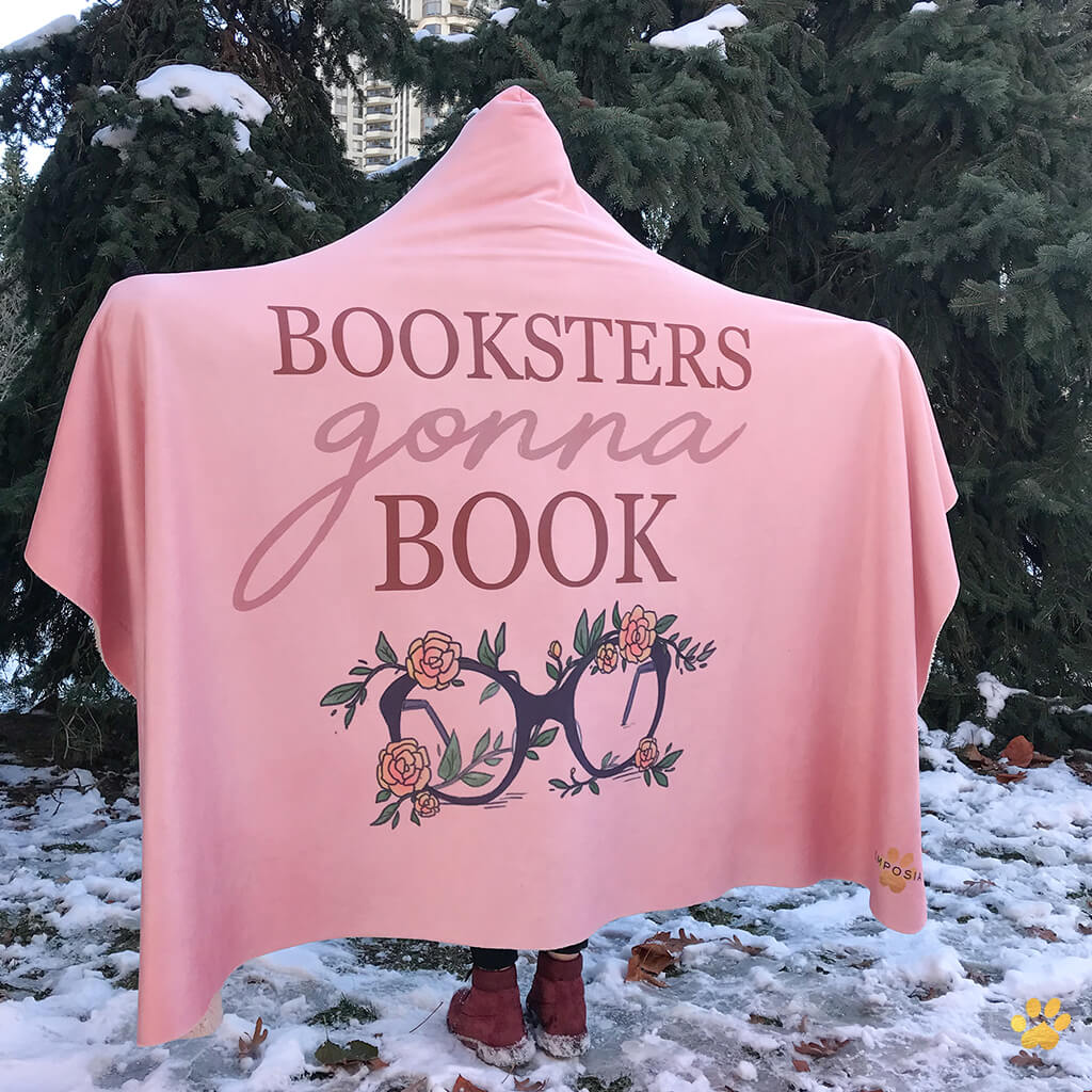 girl wearing a pink booksters gonna book emposia hooded blanket in the snow while surrounded by green trees