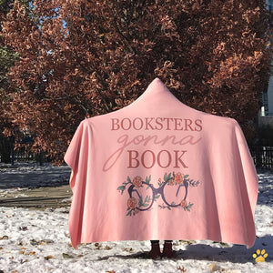 girl wearing a pink booksters gonna book emposia hooded blanket in the snow in front of a tall tree with autmn leaves